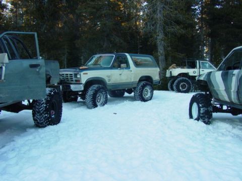 1986 Ford Bronco - Multiple off-road vehicles are parked in a snowy forest clearing.