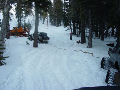 1986 Ford Bronco - Two vehicles are stuck in the snow in a wooded area, with one truck partially visible in the foreground.