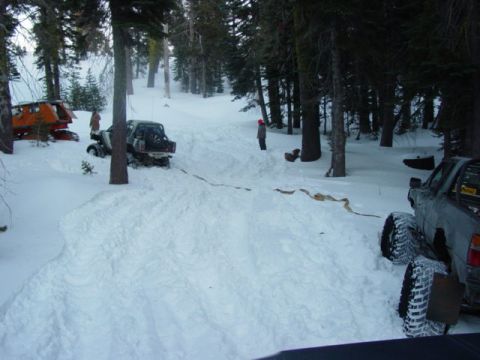 1986 Ford Bronco - Several vehicles are stuck in the snow in a forest, with one vehicle appearing to be orange and white and another a dark SUV.
