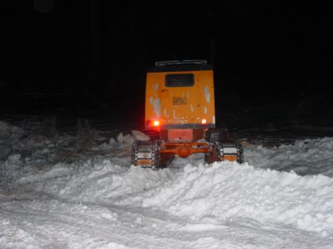 1986 Ford Bronco - An orange tracked vehicle navigates through a snowy landscape at night, its taillights glowing red.