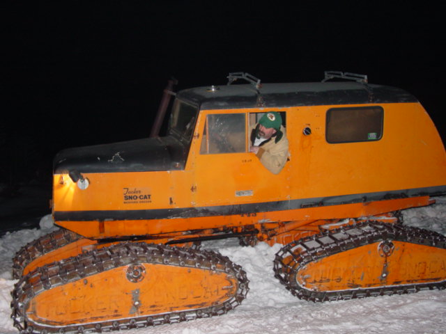guy in a green hat driving an orange Tucker Sno-Cat in the snow
