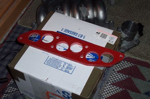 1993 Ford Taurus - A red gauge cluster mount is placed on top of shipping boxes, with automotive parts in the background.