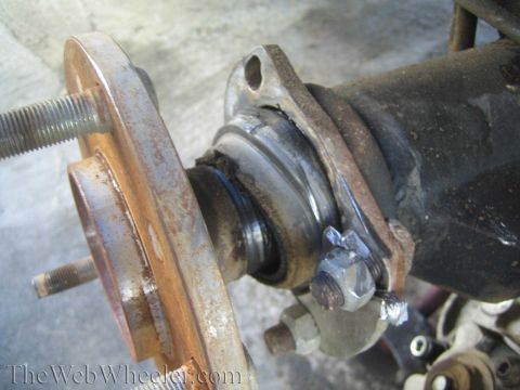 1990 Ford Bronco - Close-up of a vehicle axle shaft U-joint and rusted hub flange during a front-end teardown, watermarked TheWebWheeler.com.