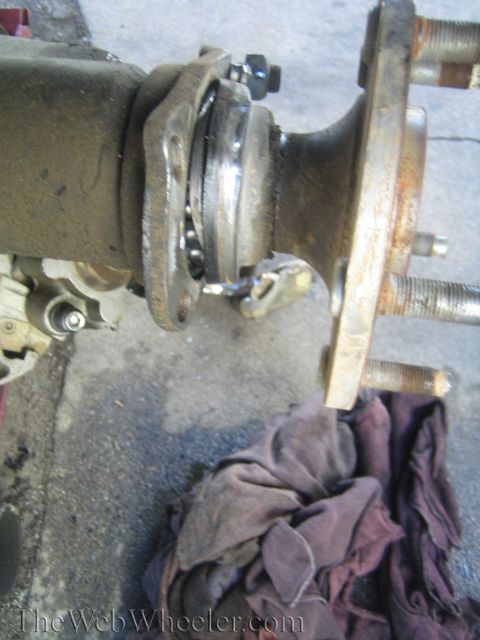 1990 Ford Bronco - vehicle axle hub and bearing assembly with protruding wheel studs, a cloth rag laid beneath, watermarked TheWebWheeler.com.