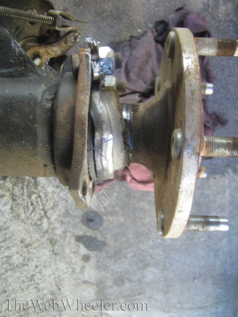 1990 Ford Bronco - Close-up of a greasy axle bearing and hub flange with threaded studs during a repair, a rag behind it, watermarked TheWebWheeler.com.