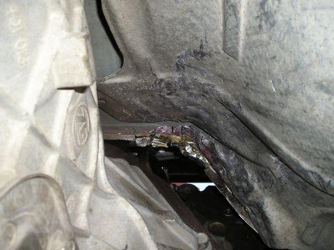 1997 Ford F-250 - The underside of a vehicle shows significant damage to a metal panel, revealing exposed layers beneath.