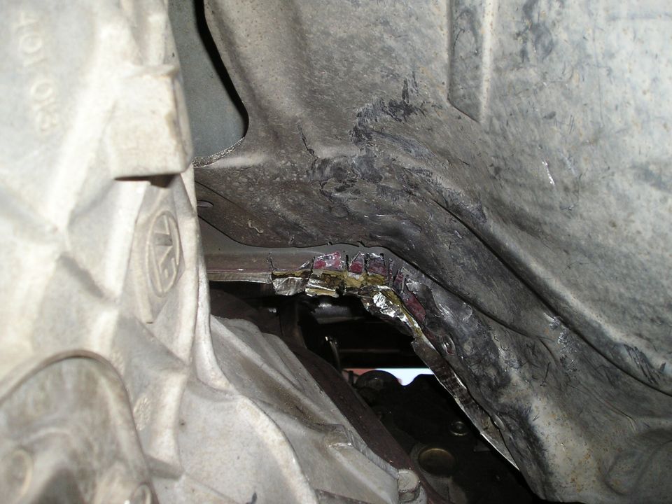 underbody of vehicle with damaged metal panel and visible transmission components