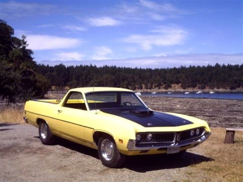 1973 Ford Ranchero - A yellow Ford Ranchero with a black hood sits parked by the water under a blue sky.
