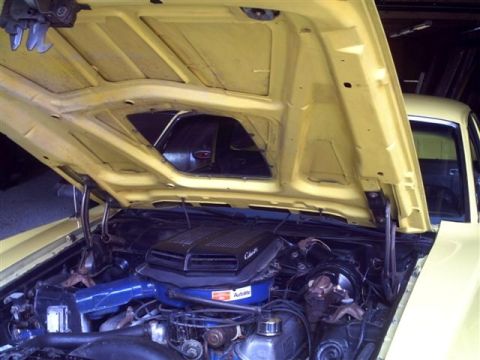 1973 Ford Ranchero - The engine bay of a yellow 1973 Ford Ranchero, viewed with the hood open, revealing the engine and air cleaner assembly.