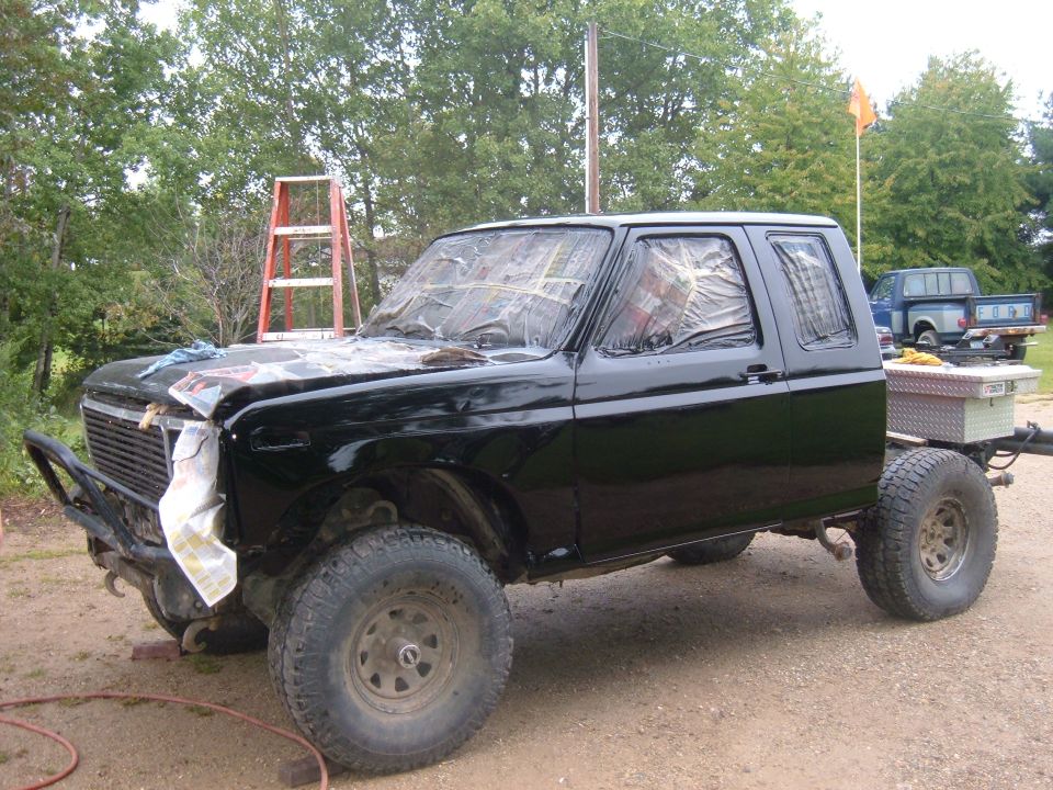 Gloss black square-body Ford 4x4 cab and chassis with masked windows on a gravel driveway
