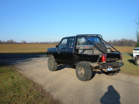 1985 Ford F-150 - This black 1985 Ford F-150 extended cab pickup truck features a custom roll cage and a spare tire mounted in the bed.