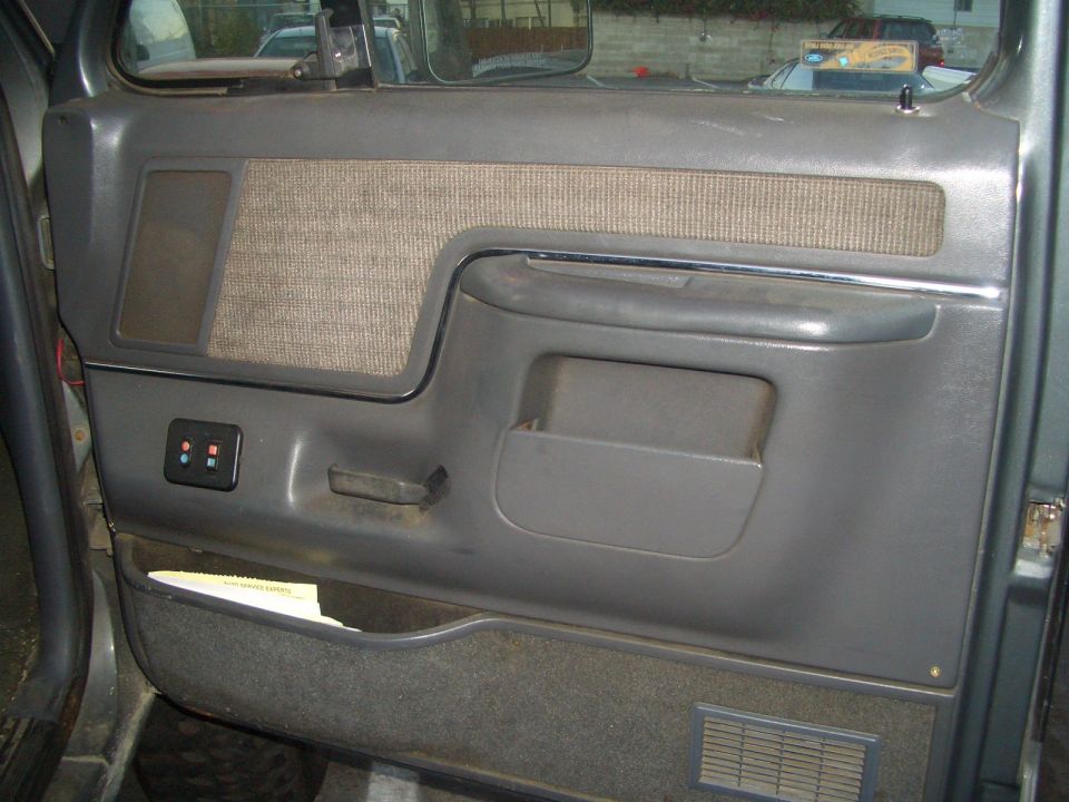 Gray interior door panel with fabric insert, storage pocket, and aftermarket switch panel