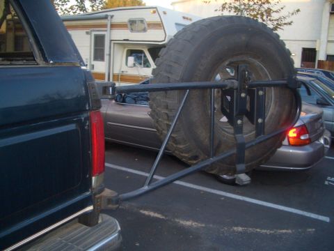 1988 Ford Bronco - The rear of a dark SUV is visible, equipped with an external spare tire carrier holding a large tire.