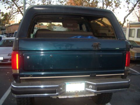 1988 Ford Bronco - Rear view of a dark green SUV, likely a Ford Bronco, parked outdoors with other vehicles nearby.