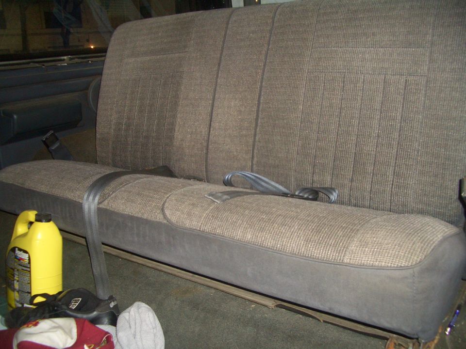1988 Ford Bronco rear bench seat with seatbelts and a yellow bottle of fluid on the floor