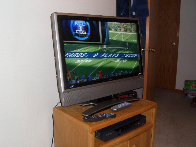 Flat-screen TV on a wood stand showing an NFL football broadcast