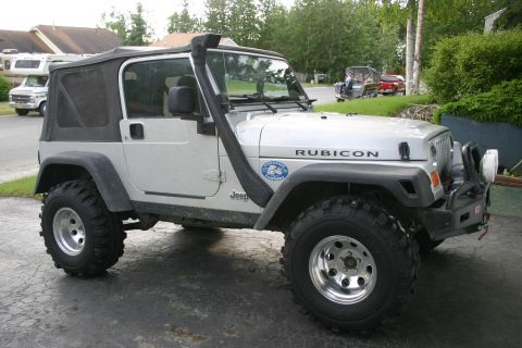 2003 Jeep TJ - A silver Jeep Wrangler is parked on a driveway, a prominent snorkel intake on the driver's side.