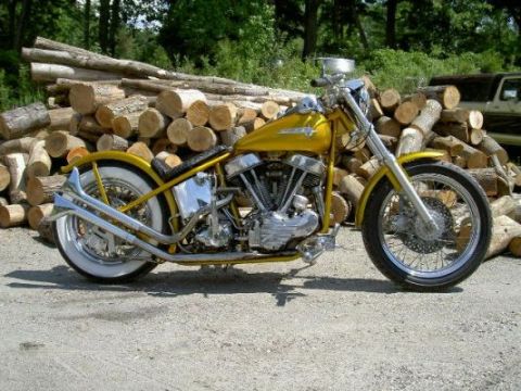 1967 Ford Ranchero - A yellow custom motorcycle with whitewall tires sits parked outdoors near a stack of cut logs.