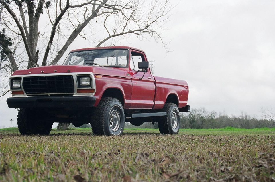 Red 1979 Ford F-150 pickup truck with a lifted suspension and off-road tires parked in a grassy field