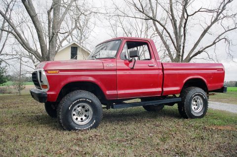 1979 Ford F-150 - This red 1979 Ford F-150 pickup truck is shown in a three-quarter front side view, parked outdoors on a grassy area.