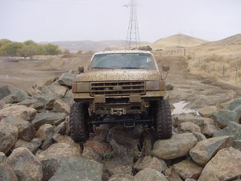 1991 Ford Bronco - This truck is navigating a rocky, off-road terrain with a muddy track ahead.