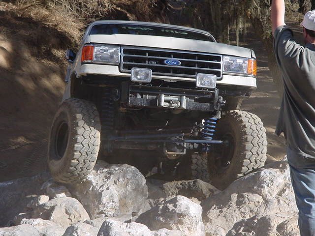 Lifted gray Ford Bronco crawling over rocks off-road, front view