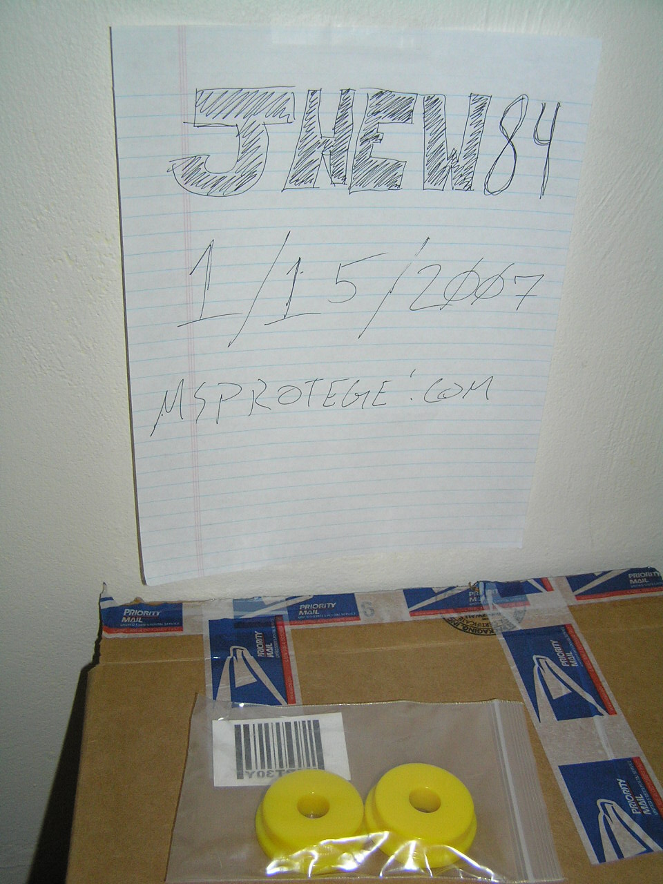 Two yellow poly bushings in a bag on a Priority Mail box with handwritten dated sign