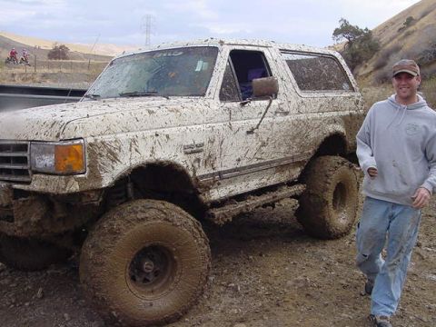 1991 Ford Bronco - A man poses next to a heavily mud-covered 1991 Ford Bronco after an off-road excursion.