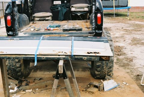 1978 Ford Bronco - The rear of a black SUV is shown with its tailgate removed, revealing the interior and seats. Tools and various parts are visible in the ca…