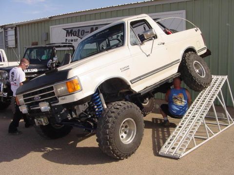 1991 Ford Bronco - A heavily modified 1991 Ford Bronco is positioned on a ramp, its lifted suspension and off-road tires.