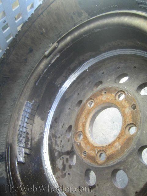 1990 Ford Bronco - Close-up of a black steel wheel rim mounted to a brake drum with a rusted hub center, watermarked TheWebWheeler.com.