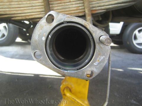 1990 Ford Bronco - End-on view into a vehicle axle tube flange bore, supported on a yellow jack with a leaf spring above, watermarked TheWebWheeler.com.