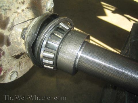 1990 Ford Bronco - Close-up of a polished tapered roller bearing seated on an axle shaft near the hub, watermarked TheWebWheeler.com.