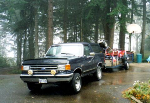 1991 Ford Bronco - A 1991 Ford Bronco tows a trailer loaded with an ATV and supplies through a wooded area.