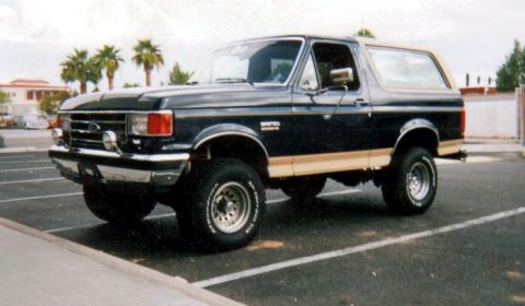 1991 Ford Bronco - Dark blue 1991 Ford Bronco with tan side trim parked in a lot.