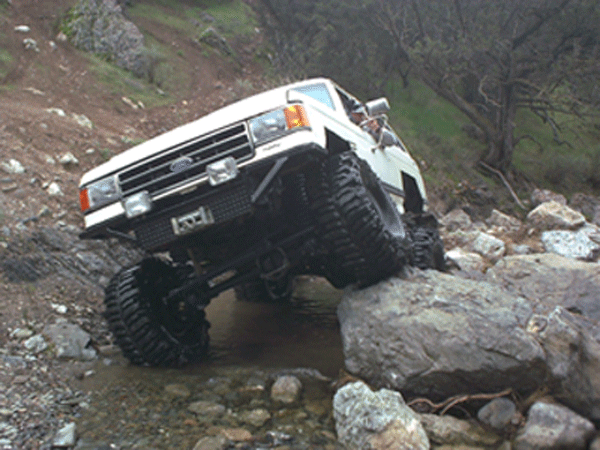 White Ford truck crawling down a rocky trail in wooded terrain
