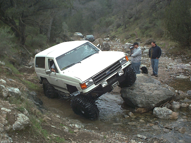 White Ford truck descending a muddy rutted trail beside a creek