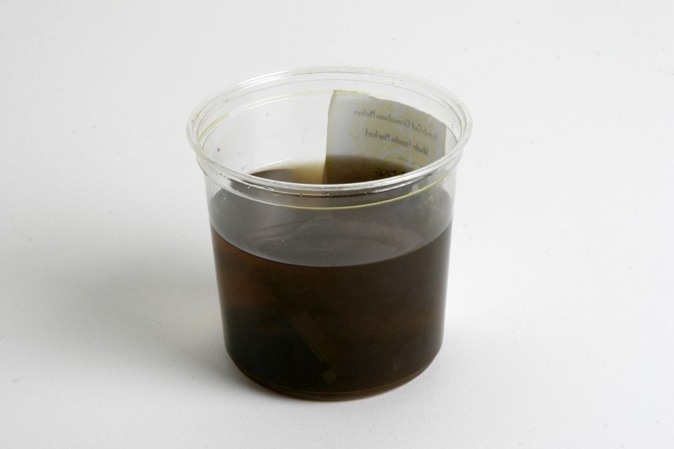 Clear plastic container half filled with dark brown liquid on a white surface