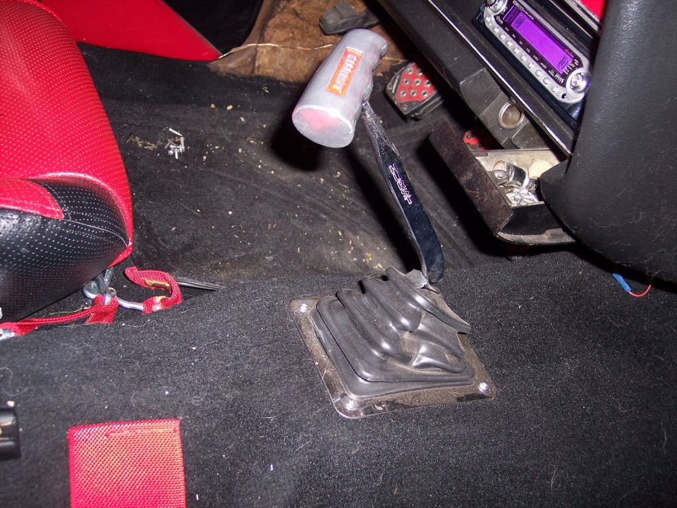Manual shifter with rubber boot and mallet knob on carpeted floor of a car interior