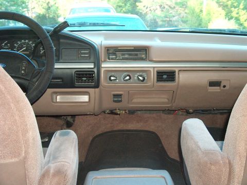 1992 Ford Bronco - The dashboard and interior of a 1992 Ford Bronco are visible, with a light blue vehicle in the background.
