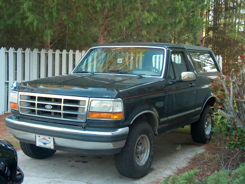 1992 Ford Bronco - A black 1992 Ford Bronco is parked in front of a white picket fence and trees.