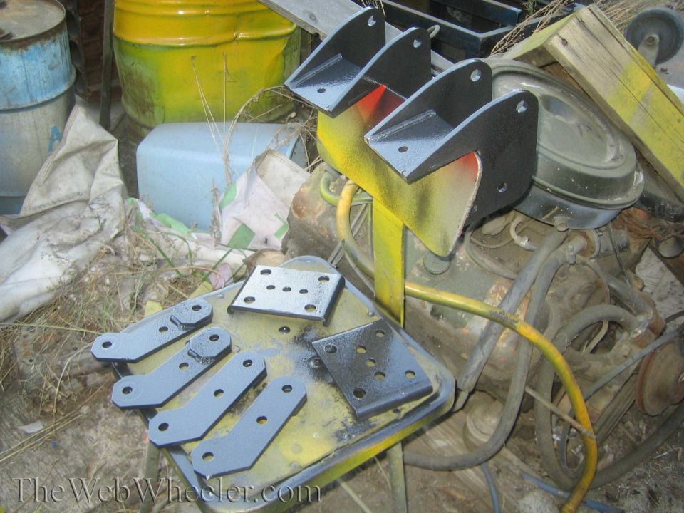 Freshly painted black leaf-spring hangers and shackle plates drying on a shop cart