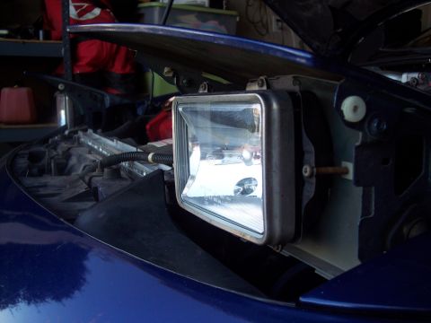 1995 Ford Probe - Close-up of a car's headlight assembly removed from the vehicle, revealing the mounting bracket and wiring harness.