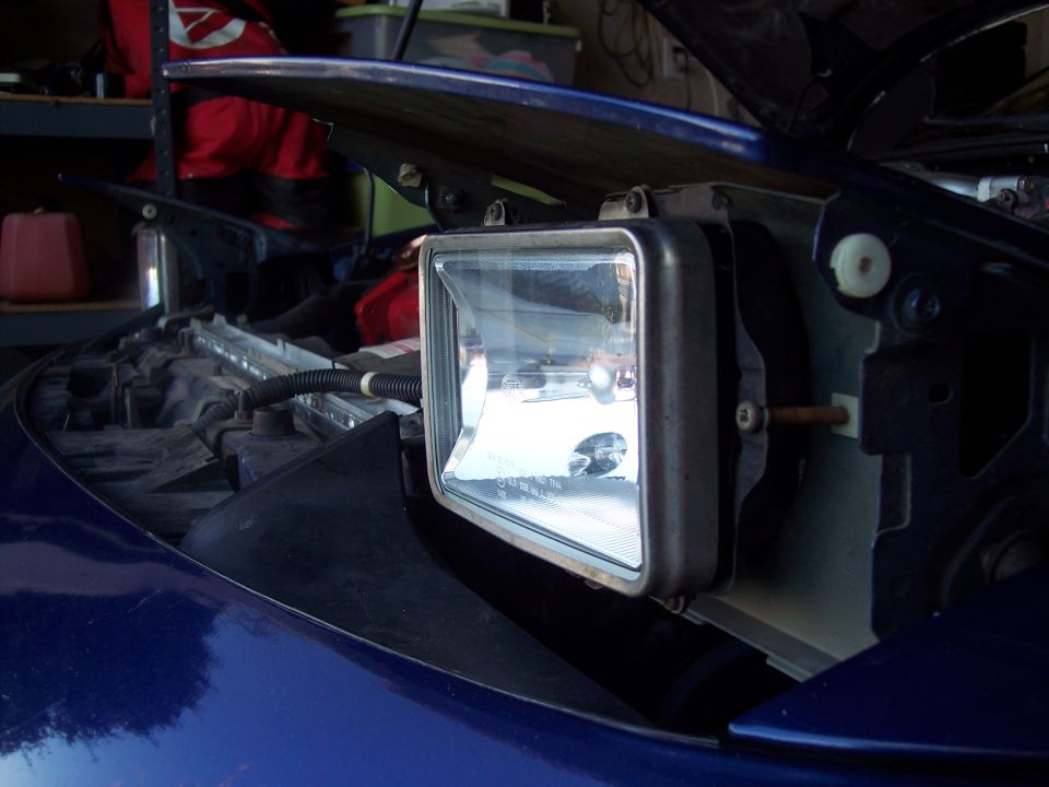 Blue car's front headlight assembly removed, showing internal components and wiring