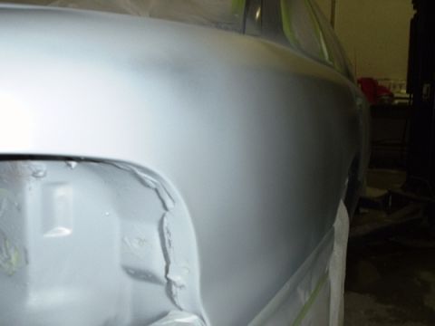 1996 Ford Crown Victoria - A car's rear quarter panel is prepped for refinishing, revealing damage on the lower section.
