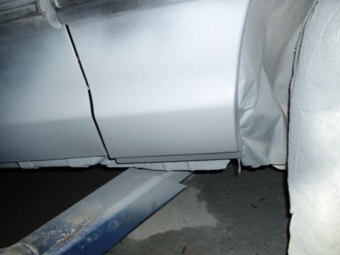 1996 Ford Crown Victoria - Close-up view of a car's side panel and rocker, prepped for refinishing with a gray primer coat.