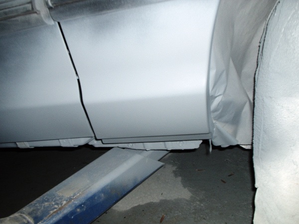 Gray primer on car door seam and rocker panel, covered in protective sheeting