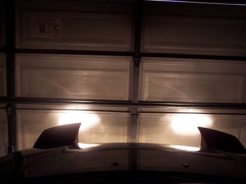 1995 Ford Probe - Headlights illuminated on a car hood with two distinct fins, parked in front of a garage.