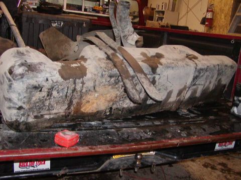 1979 Ford F-150 - A dirty fuel tank is secured in the bed of a red pickup truck.