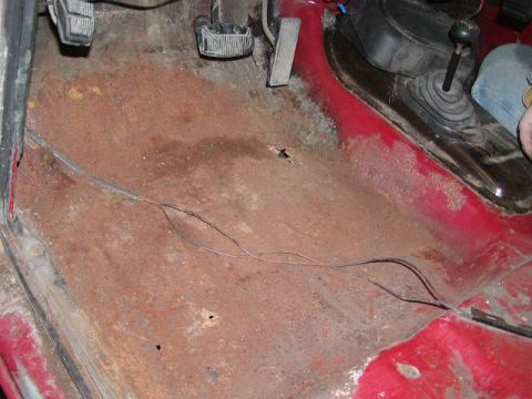 1979 Ford F-150 - The interior floor of a vehicle shows significant rust damage and exposed wiring.